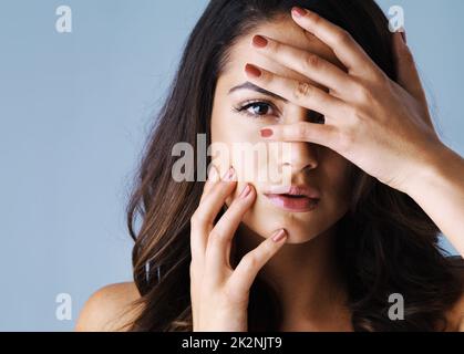 Perfekte Nägel, perfektes Make-up, perfektes Haar. Studioaufnahme einer attraktiven jungen Frau, die ihr Gesicht berührt, um ihre wunderschönen Nägel vor grauem Hintergrund zu zeigen. Stockfoto