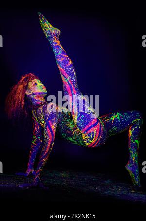 Schätze im Dunkeln. Ganzkörperaufnahme einer jungen Frau, die mit Neonfarbe auf ihrem Gesicht posiert. Stockfoto