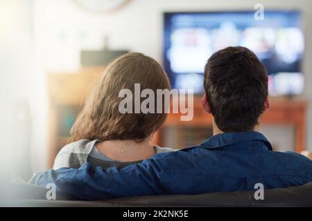 TV und Chill. Rückansicht eines entspannten jungen Paares, das zu Hause fernsieht. Stockfoto