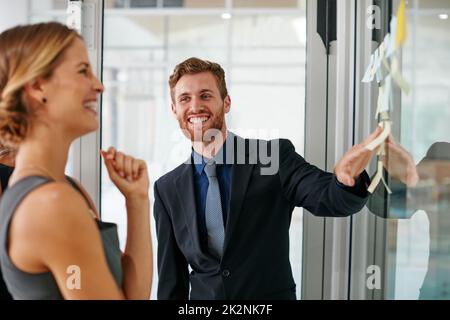 Das Beste aus ihren Problemlösungsfähigkeiten zu machen. Aufnahme von Mitarbeitern, die während einer Brainstorming-Sitzung Haftnotizen gegen die Wand verwendeten. Stockfoto