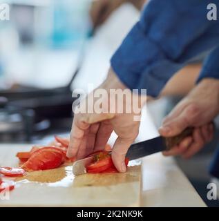 Schneiden und Würfeln. Aufnahme eines nicht identifizierbaren Mannes, der zu Hause in seiner Küche Tomaten zerschnitt. Stockfoto