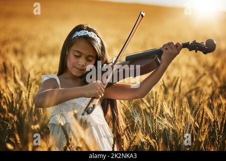 Die Natur hat Musik für diejenigen, die zuhören. Aufnahme eines niedlichen kleinen Mädchens, das in einem Kornfeld auf der Geige spielt. Stockfoto