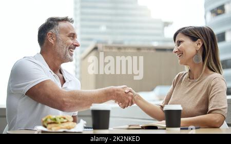 Geschäftstreffen wurden beim Mittagessen besser. Aufnahme von zwei Geschäftsleuten, die sich beim Mittagessen vor einem Büro die Hände schüttelten. Stockfoto