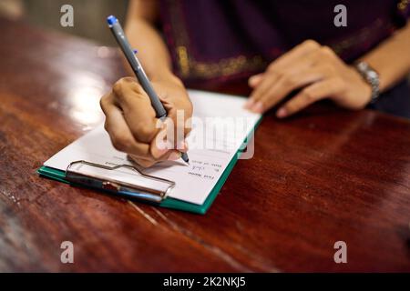 Check-in-Zeit. Nahaufnahme einer Frau, die ein Hotel-Check-in-Formular auf einem Clipboard an einem Hotelrezeptionsschalter ausfüllt. Stockfoto