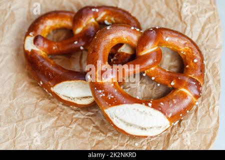 Zwei hausgemachte, frisch gebackene, weiche Brezeln auf braunem Papier. Traditionelle bayerische Brezel zum Oktoberfest. Nahaufnahme Stockfoto