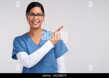 Ärzte eliminieren die nrn auf ihren freien Stellen Zeichen zu existieren. Porträt einer jungen Ärztin, die Brille und Peeling trägt und auf ihre linke Seite zeigt, vor weißem Hintergrund. Stockfoto