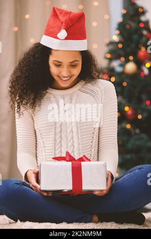 Lassen Sie das Weihnachtsgeschenk Ihr Herz mit Glück erfüllen. Aufnahme einer glücklichen jungen Frau, die zu Weihnachten zu Hause Geschenke eröffnet. Stockfoto