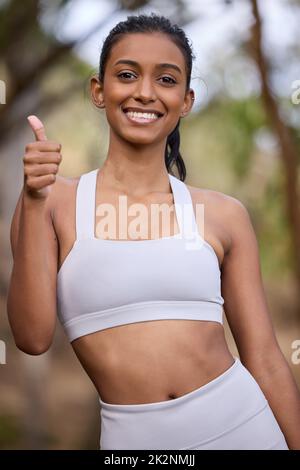 Es fühlt sich toll an, fit zu sein. Porträt einer sportlichen jungen Frau mit Daumen nach oben im Freien. Stockfoto