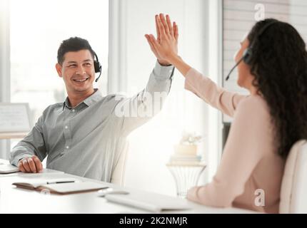 Gute Arbeit. Aufnahme von zwei jungen Call Center-Agenten, die sich in einem Büro bei der Arbeit gegenseitig eine hohe fünf geben. Stockfoto