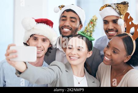 In den Weihnachtsgeist eintauchen. Aufnahme einer Gruppe von Geschäftsleuten, die ein Selfie bei der Arbeit machen. Stockfoto