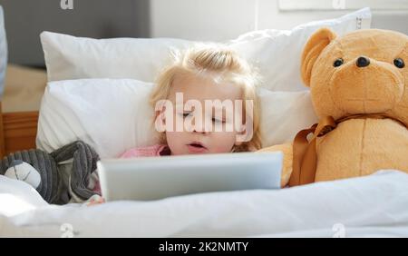 Ich kenne nur den Kinderreim zum Spielen. Aufnahme eines entzückenden kleinen Mädchens, das mit einem digitalen Tablet im Bett liegt. Stockfoto