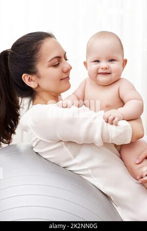 Mutter spielt mit ihrem kleinen Mädchen auf einem Fitnessball Stockfoto