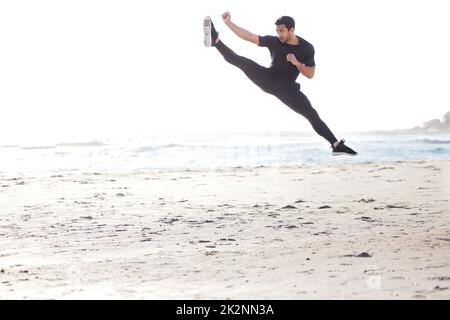 In hohen Gang zu treten. Ganzkörperaufnahme eines hübschen jungen Athleten, der am Strand trainieren soll. Stockfoto