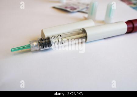 Injektionsspritze auf einem weißen Tisch mit Ersatznadeln im Hintergrund. Diabetes mellitus. Stockfoto