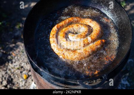 Hausgemachte Schweinewürste in einer rustikalen Bratpfanne mit verschiedenen Gewürzen. Erholung im Freien. Stockfoto