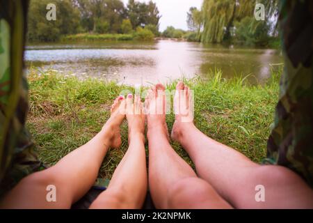 Ein kleines Zelt am See, eine Übernachtung und die Füße eines jungen Paares Stockfoto