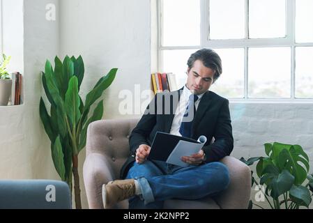 Junger Geschäftsmann, der Papierkram liest, zu Hause auf der Couch liegt und sich das Finanzanalysedokument für die Karriereentwicklung anschaut. Finanzbericht des Unternehmens Stockfoto