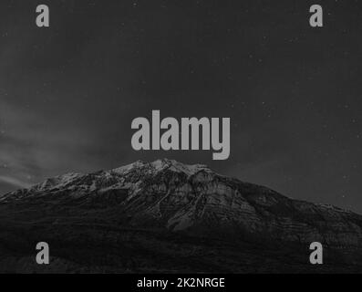 Eine Graustufenaufnahme des schneebedeckten Gipfels eines Berges mit Wolken darüber Stockfoto