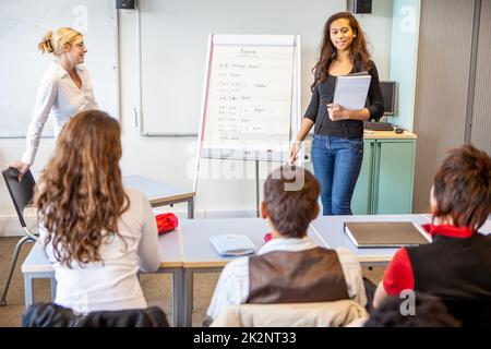 Teenager: Die Klasse ansprechen. Eine Schülerin, die ihren Klassenkameraden eine Präsentation gibt. Aus einer Reihe verwandter Bilder. Stockfoto
