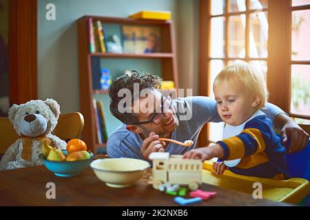 Er hat die alleinerziehende Erziehung unter Kontrolle. Ausgeschnittene Aufnahme eines alleinerziehenden Vaters, der seinen Sohn zu Hause füttert. Stockfoto