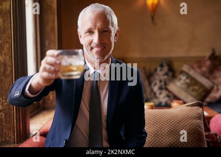 Heben Sie ein Glas mit mir Porträt eines gut gekleideten, reifen Mannes, der nach der Arbeit mit einem Glas Whiskey in einer Bar anstoßen kann. Stockfoto