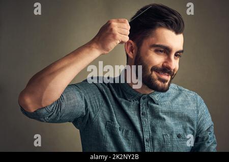 Haben Sie jemals etwas so schönes gesehen? Studioaufnahme eines hübschen jungen Mannes, der seine Haare vor einem grauen Hintergrund kämmt. Stockfoto