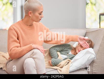 Heute gibt es keine Schule für Sie. Aufnahme einer Mutter, die zu Hause auf dem Sofa die Temperatur ihrer Töchter überprüft. Stockfoto