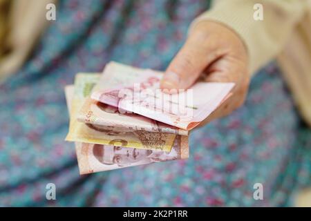 Ältere Patientin aus Asien, die Geldscheine in der Hand hält, Lebenshaltungskosten und medizinische Versorgung. Stockfoto