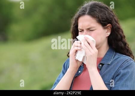 Eine kranke Frau, die in einem Park auf Gewebe bläst Stockfoto