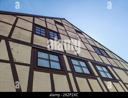 Blick aus einem niedrigen Winkel auf die Fassade des Hauses mit gelbem Stein und Halbholzbaumholz am blauen Himmel. Stockfoto