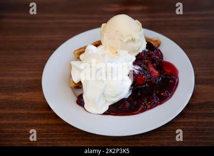 Ein Teller mit Waffeln, Vanillesauce, Sahne und Kirschen. Stockfoto