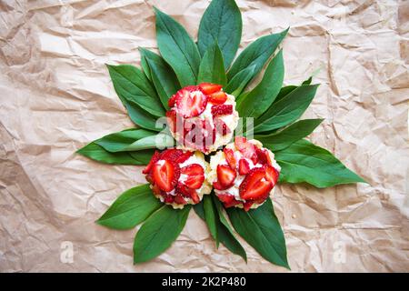 Schöne und helle kleine Kuchen mit Erdbeeren liegen auf grünen Blättern Stockfoto