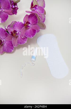 Hygieneartikel während Ihrer Periode wird ein Tampon oder Pad mit einer lila Orchideenblume platziert. Stockfoto