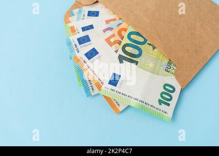 Ein Cache mit Euro-Geld, in Banknoten mit 100 Stückelungen, die aus einem Umschlag auf blauem Hintergrund kommen. Das Konzept von Gehalt, Bestechung, Kredit, Schulden, Gewinn. Stockfoto