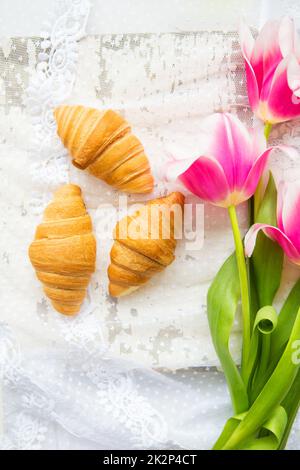 Drei Croissants und leuchtend rosa Tulpen auf Spitze Tischdecke, close-up Stockfoto