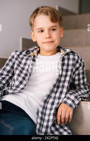 Stilvoller Teenager-Typ lächelt, während er für ein schönes Foto posiert, während er auf der Treppe sitzt. Stockfoto