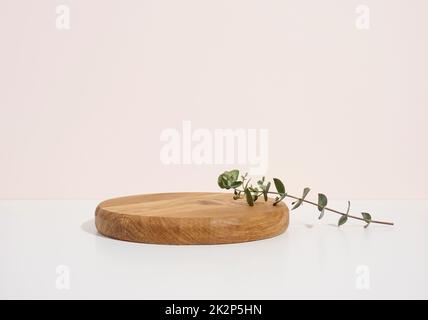 Bühne für die Präsentation von Produkten, Kosmetik mit einem runden Holzpodium und einem grünen Eukalyptusblatt Stockfoto