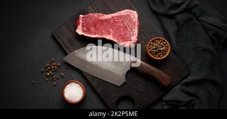 Frisches rohes Stück Rindfleisch, Striploin-Steak auf schwarzem Hintergrund, Draufsicht. Marmoriertes Stück Fleisch Stockfoto