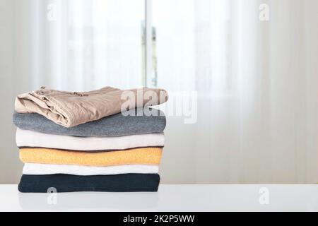 Ein Stapel Frühlingsbekleidung. Ein Haufen bunter gestrickter, gemütlicher Pullover aus warmem Kaschmir oder Pullover auf dem Tisch vor abstraktem, hellem Hintergrund. Platz für die Montage des Displays. Wunderschöne Kulisse. Stockfoto