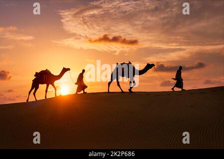 Indische Kameltreiber mit Kamelsilhouetten in Dünen bei Sonnenuntergang. Jaisalmer, Rajasthan, Indien Stockfoto