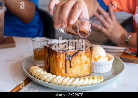 Honigtoast mit Bananenscheiben, Vanille und Schokoladeneis auf hellgrüner Keramikplatte. Stockfoto