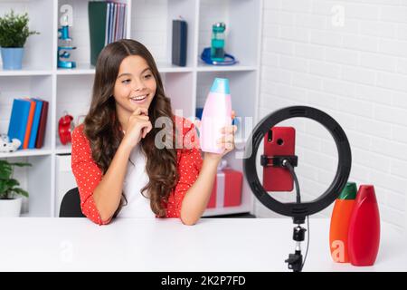 Teenager-Blogger halten Haarspülung oder Shampoo-Flasche machen Video, Kind Vlogger Influencer aufzeichnen Inhalte. Kinderblogger zeichnet Videos auf dem Handy auf Stockfoto