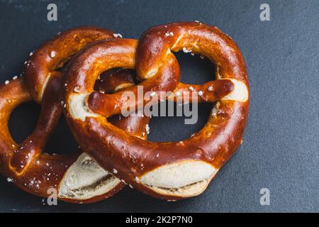 Zwei hausgemachte, frisch gebackene, weiche Brezeln auf schwarzem Hintergrund. Traditionelle bayerische Brezel zum Oktoberfest. Draufsicht, Kopierbereich Stockfoto