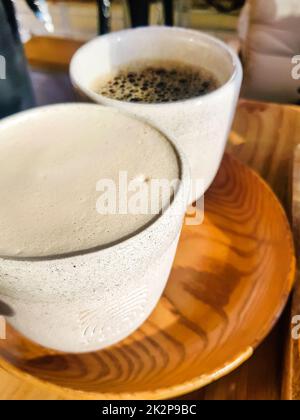Cappuccino mit duftendem Milchschaum und schwarzem Americano auf einem Holztablett. Blick von oben. Kaffee für zwei. Leckerer frisch gebrühter Kaffee zum Frühstück im Café Stockfoto
