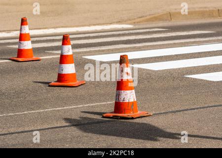 Verkehrskegel mit orangefarbenen und weißen Streifen, die während der Straßenbauarbeiten auf grauem Asphalt auf der Straße stehen Stockfoto