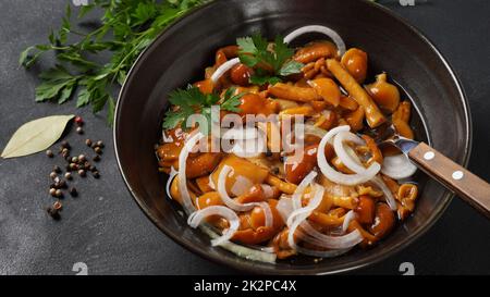 Marinierter Wildhonigpilz Armillaria mellea Pilze mit Gewürzen und Zwiebeln in der Schüssel. Stockfoto