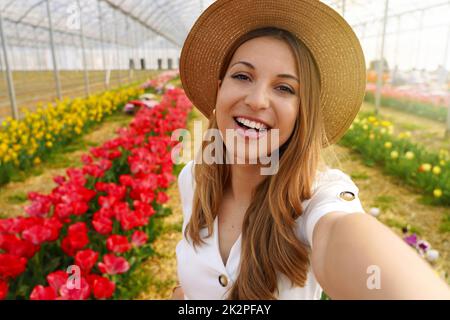 Brasilianisches Mädchen lacht dabei Selbstporträt zwischen Tulpen. Content Creator zeigt Greenhouse im Frühling in ihren Geschichten auf der mobilen App. Stockfoto