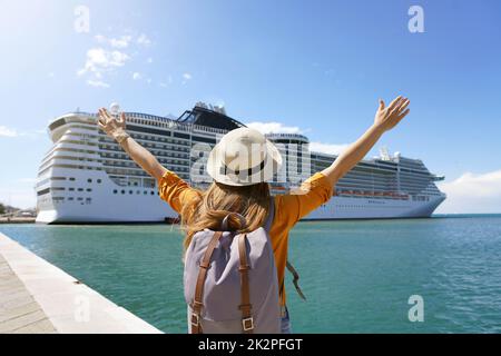 Rückansicht eines Reisenden Mädchens mit erhobenen Armen, das vor einem großen Kreuzfahrtschiff stand Stockfoto