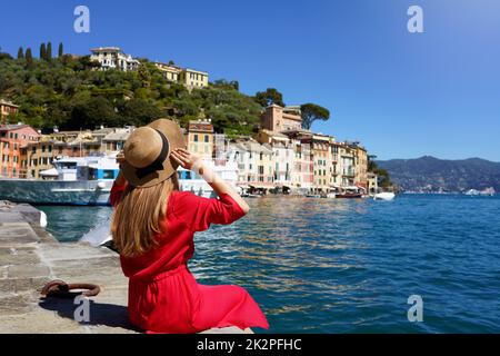Besuch Von Portofino, Italien. Ein Touristenmädchen im Urlaub, das im Hafen von Portofino sitzt. Attraktive junge romantische Frau, die den Blick auf das malerische Dorf Portofino in Italien genießt. Stockfoto