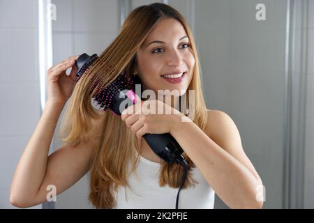 Die junge Frau hält einen runden Bürstenfon, um das Haar zu Hause auf einfache Weise zu stylen Stockfoto